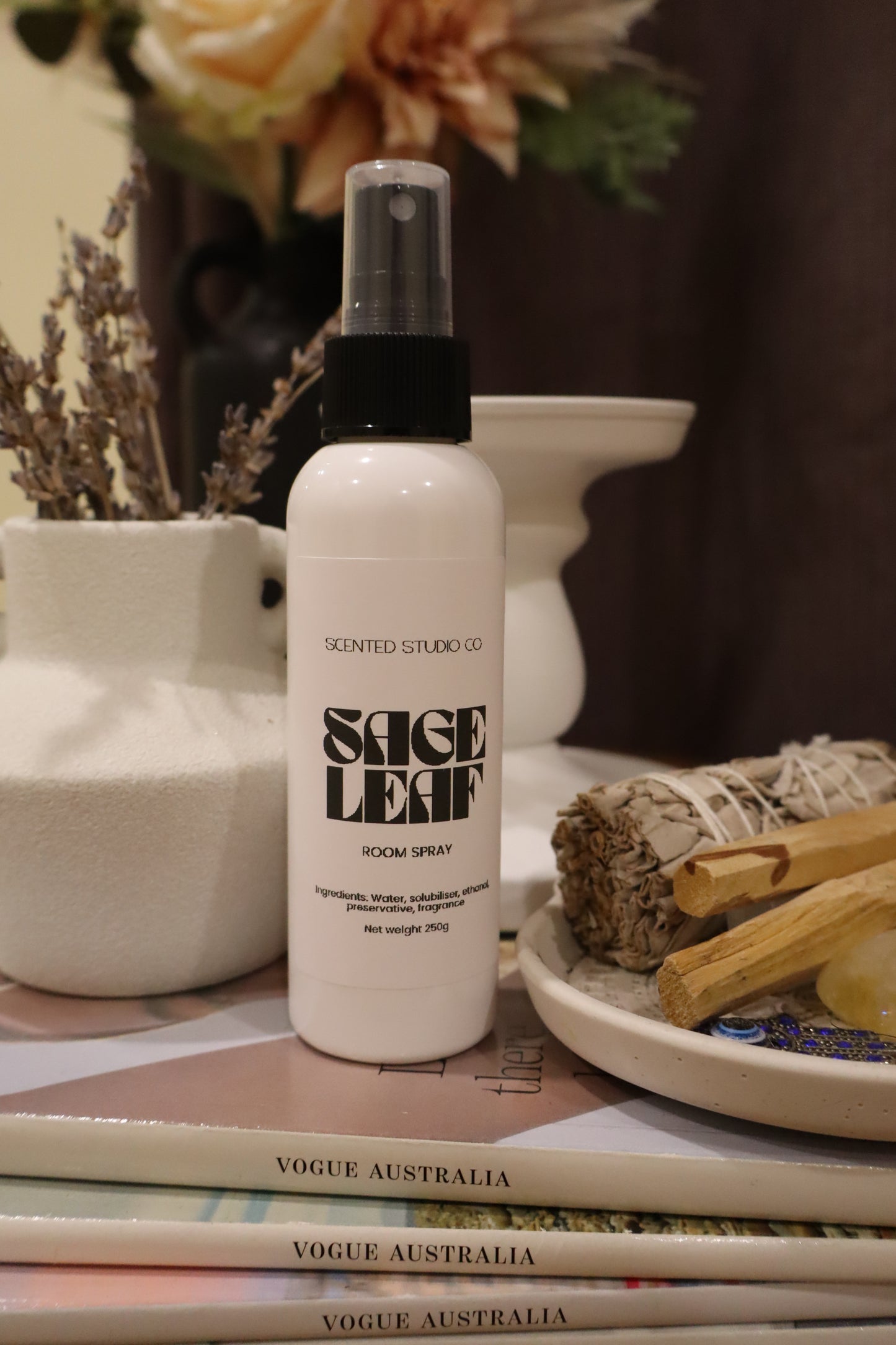 White spray bottle labeled 'Sage Leaf' on a shelf with books and decorative items.