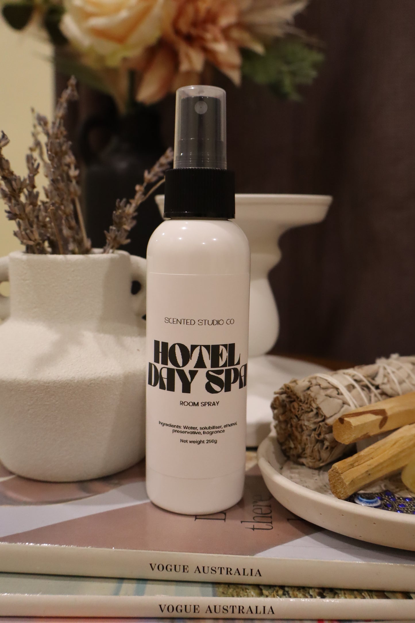 White spray bottle with black text on a surface with books and decorative items.