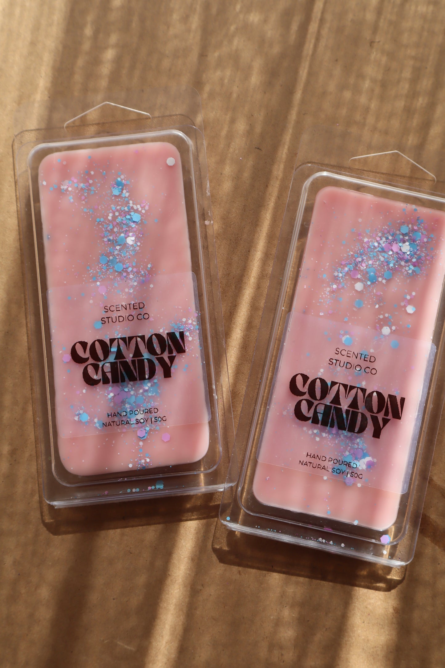 Two pink 'Cotton Candy' scented wax melts in packaging on a wooden surface.