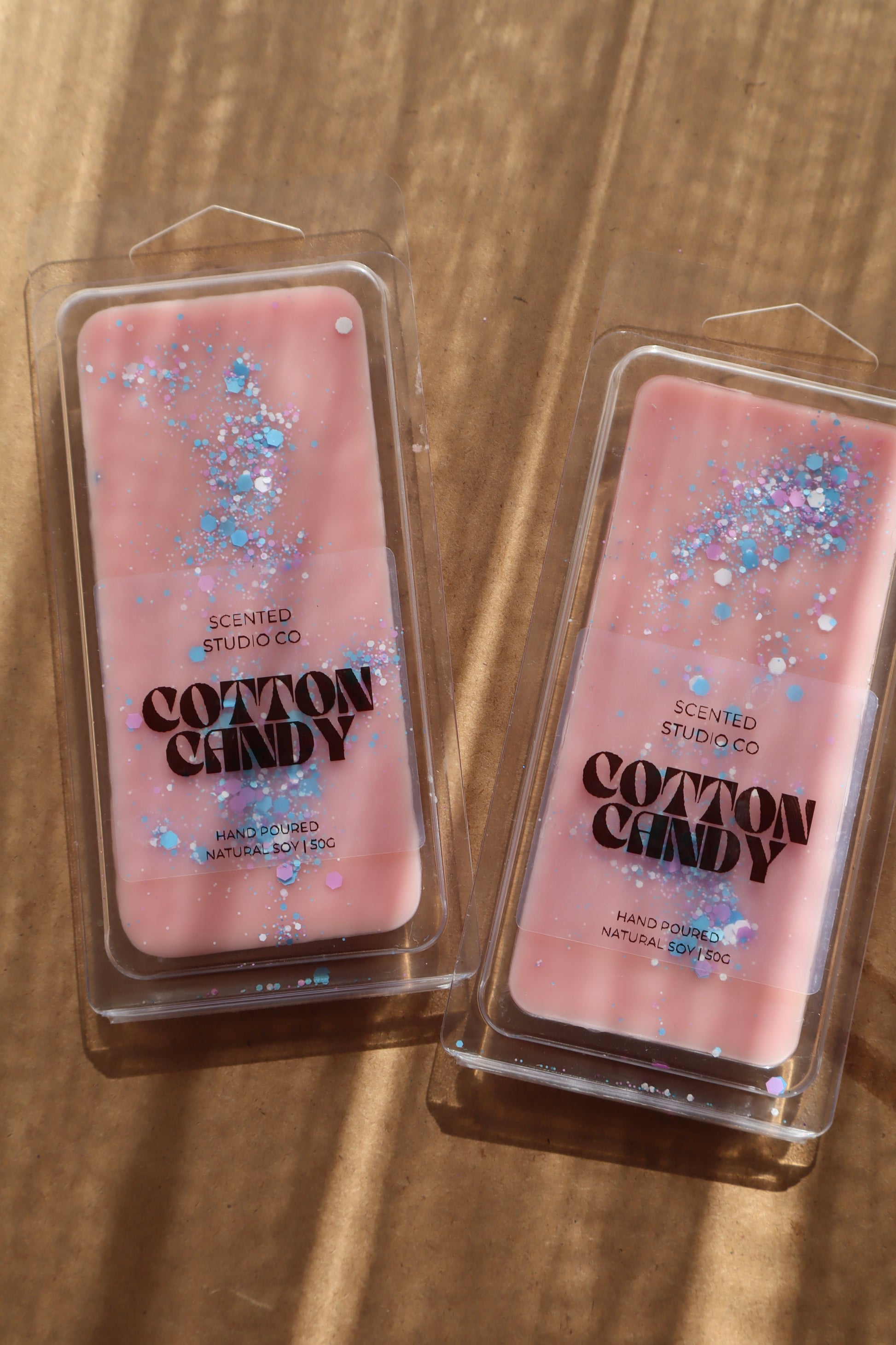 Two pink 'Cotton Candy' scented wax melts in packaging on a wooden surface.