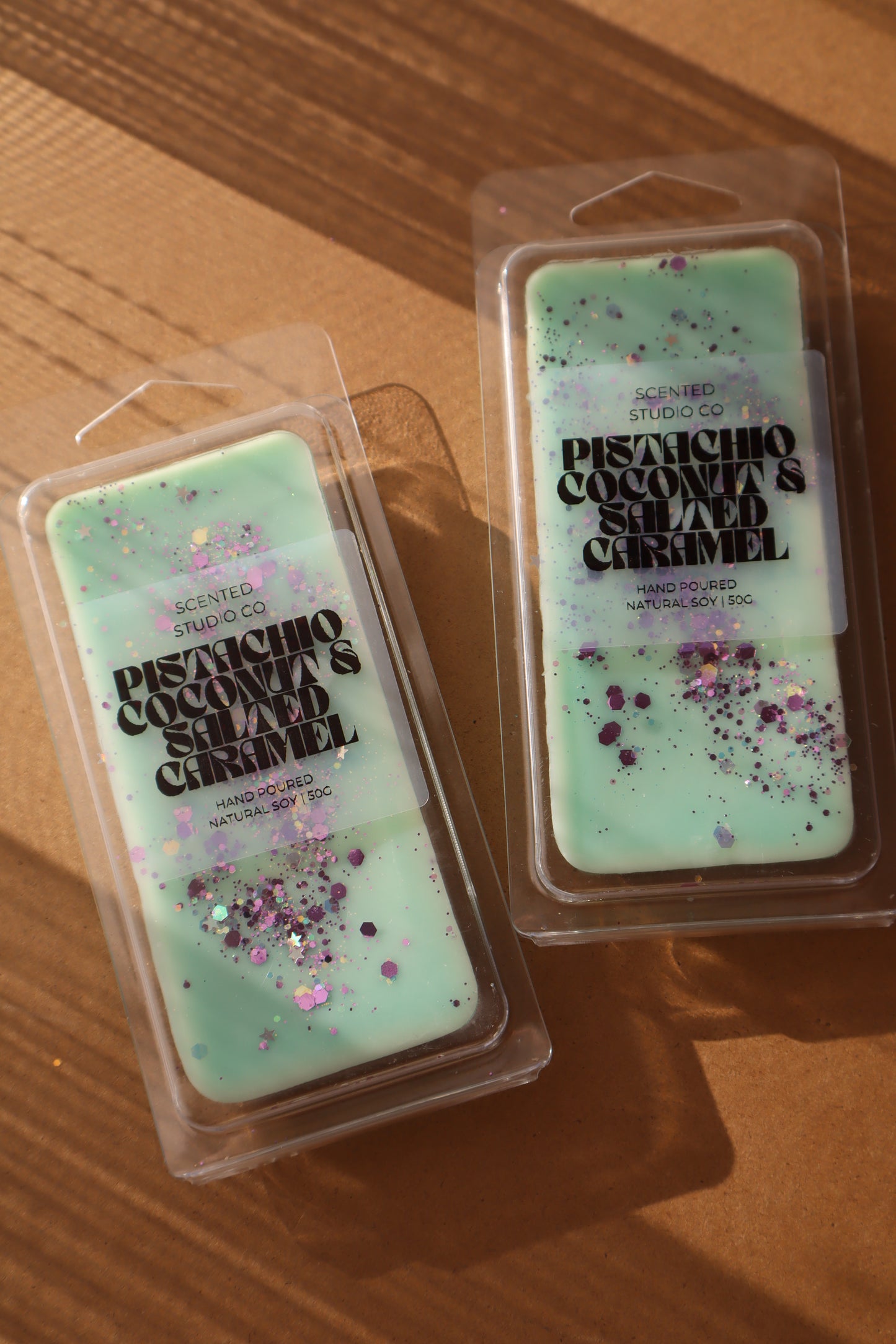 Two green wax melts with glitter in clear packaging on a wooden surface